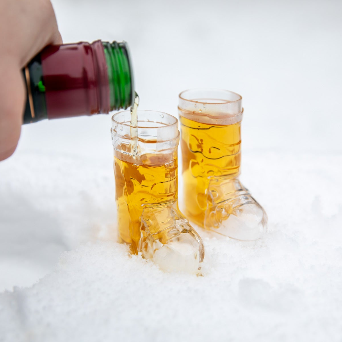 Person pouring liquid from a bottle into two glasses on snow